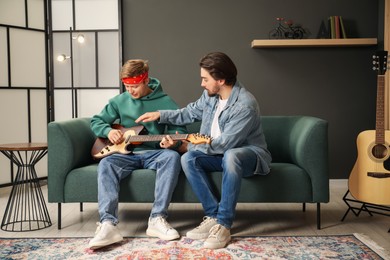 Photo of Tutor teaching man to play guitar on sofa indoors