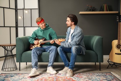 Photo of Tutor teaching man to play guitar on sofa indoors
