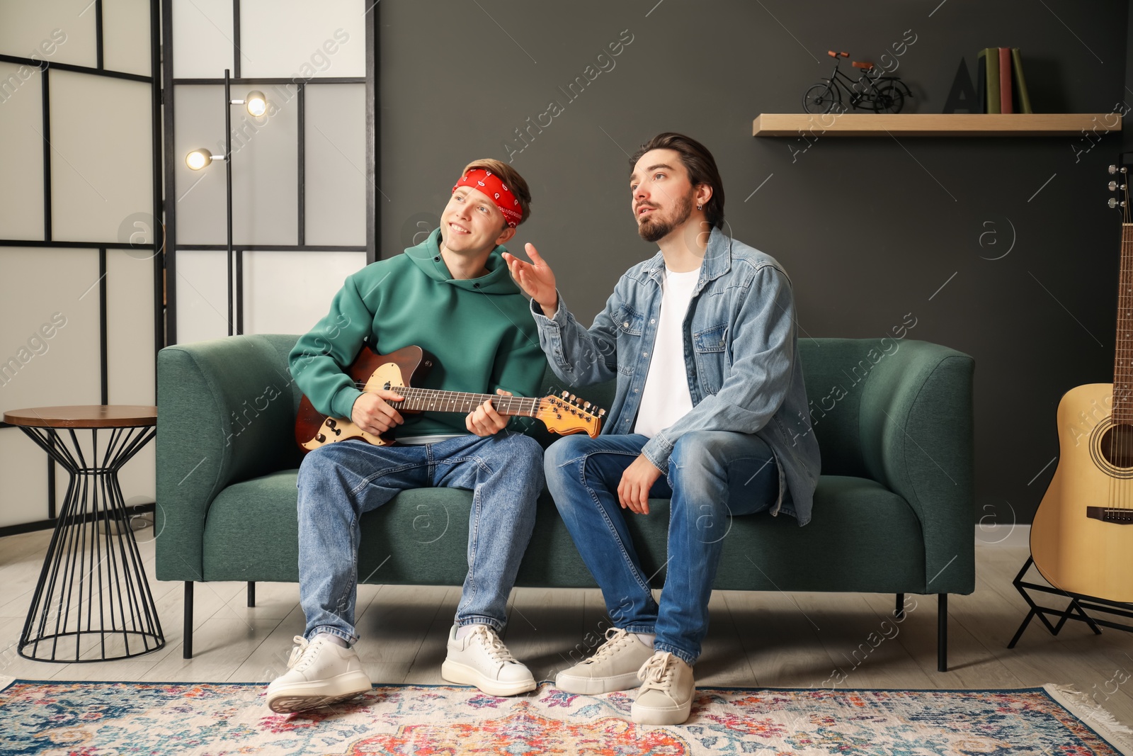 Photo of Tutor teaching man to play guitar on sofa indoors