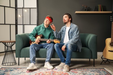 Photo of Tutor teaching man to play guitar on sofa indoors