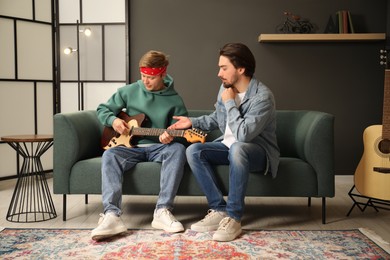 Photo of Tutor teaching man to play guitar on sofa indoors
