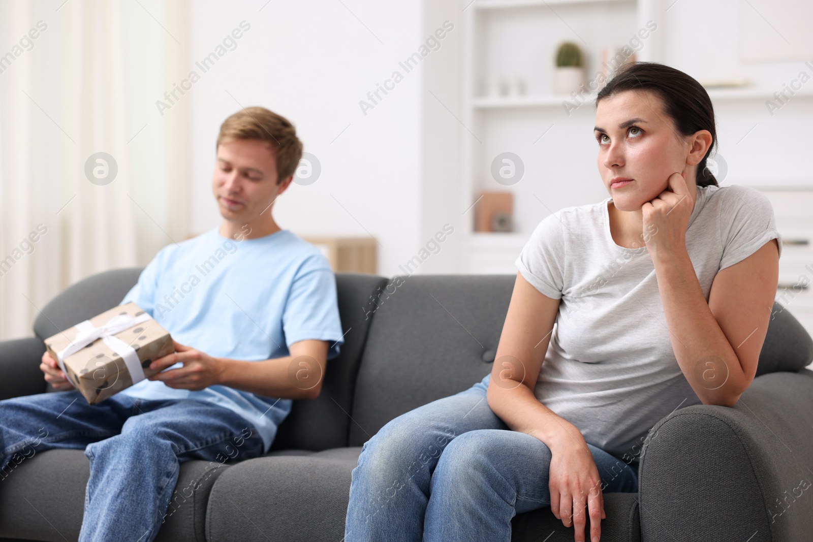 Photo of Woman feeling jealous of man receiving gift at home, selective focus