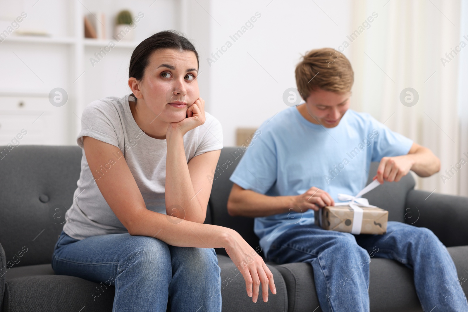 Photo of Woman feeling jealous of man receiving gift at home, selective focus