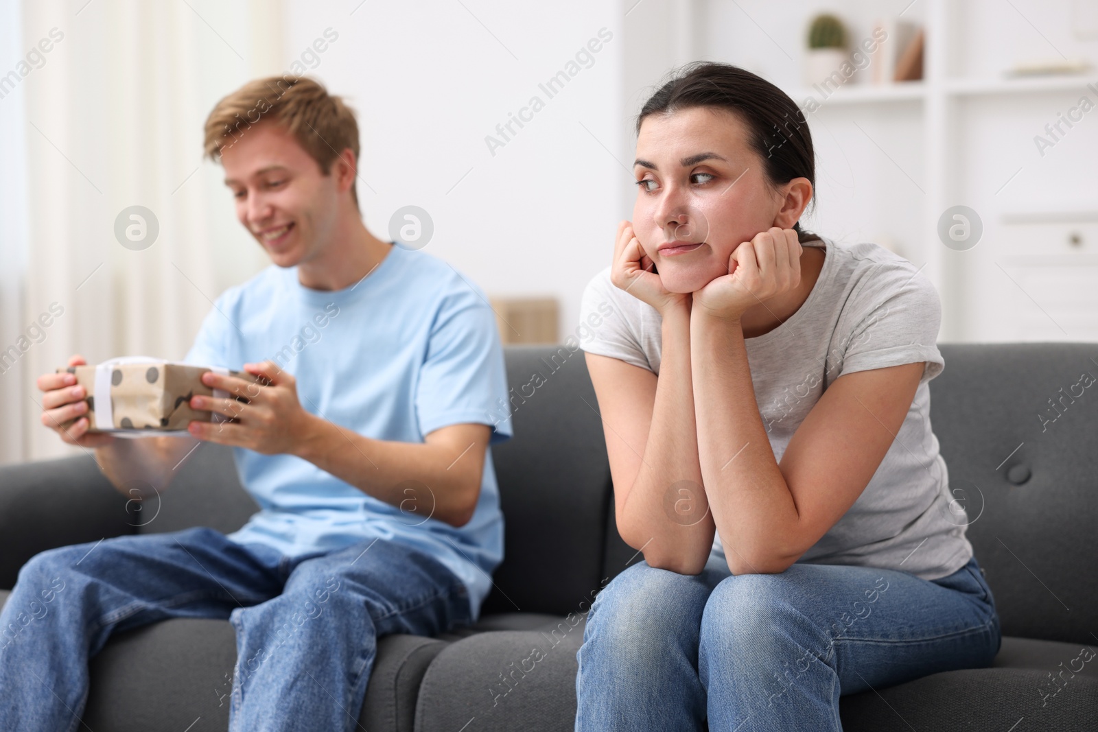 Photo of Woman feeling jealous of man receiving gift at home, selective focus