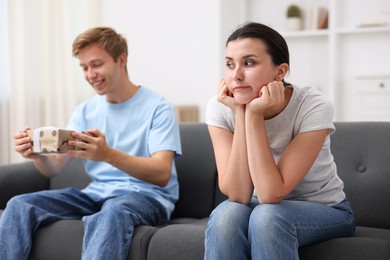 Photo of Woman feeling jealous of man receiving gift at home, selective focus