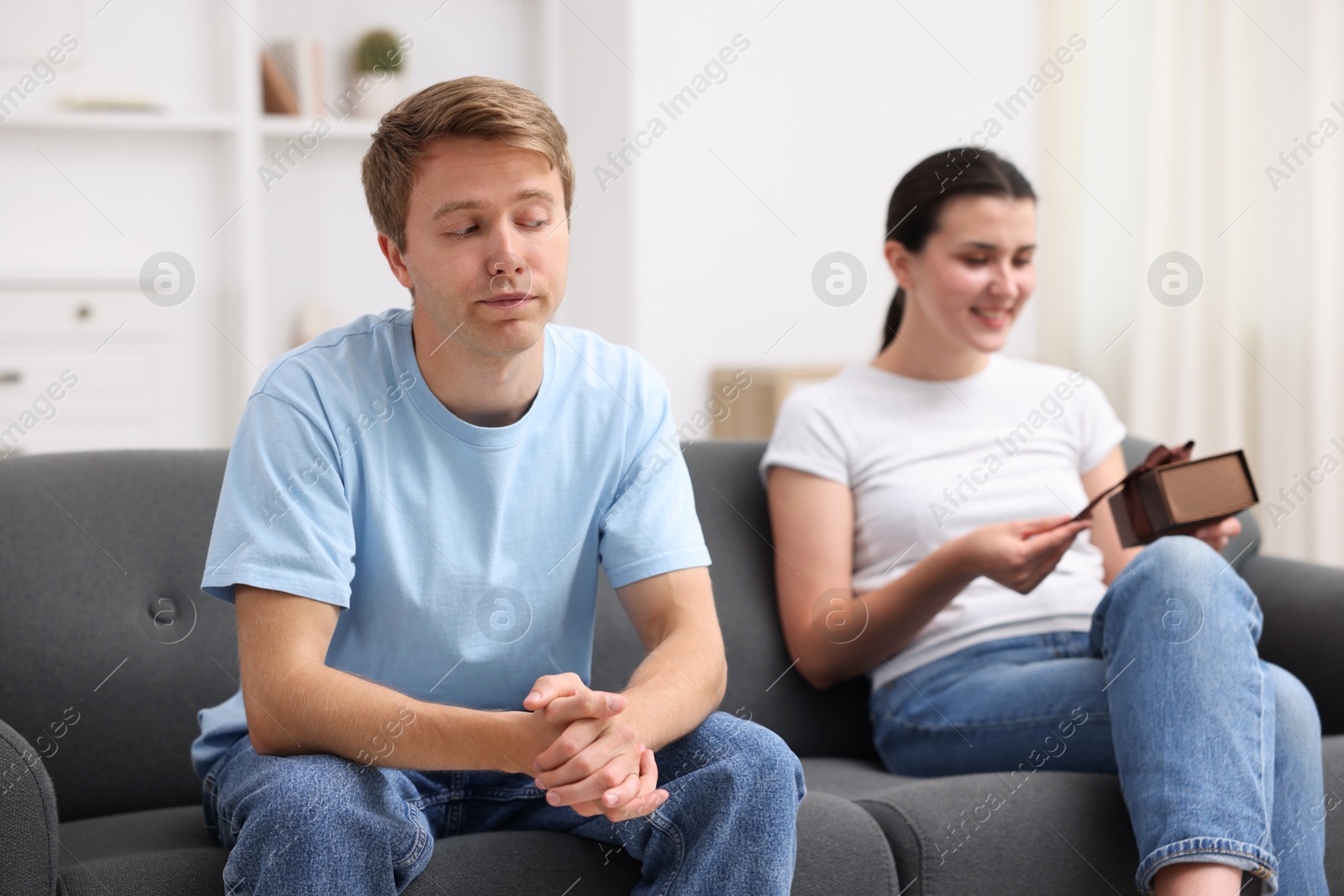 Photo of Man feeling jealous of woman receiving gift at home, selective focus