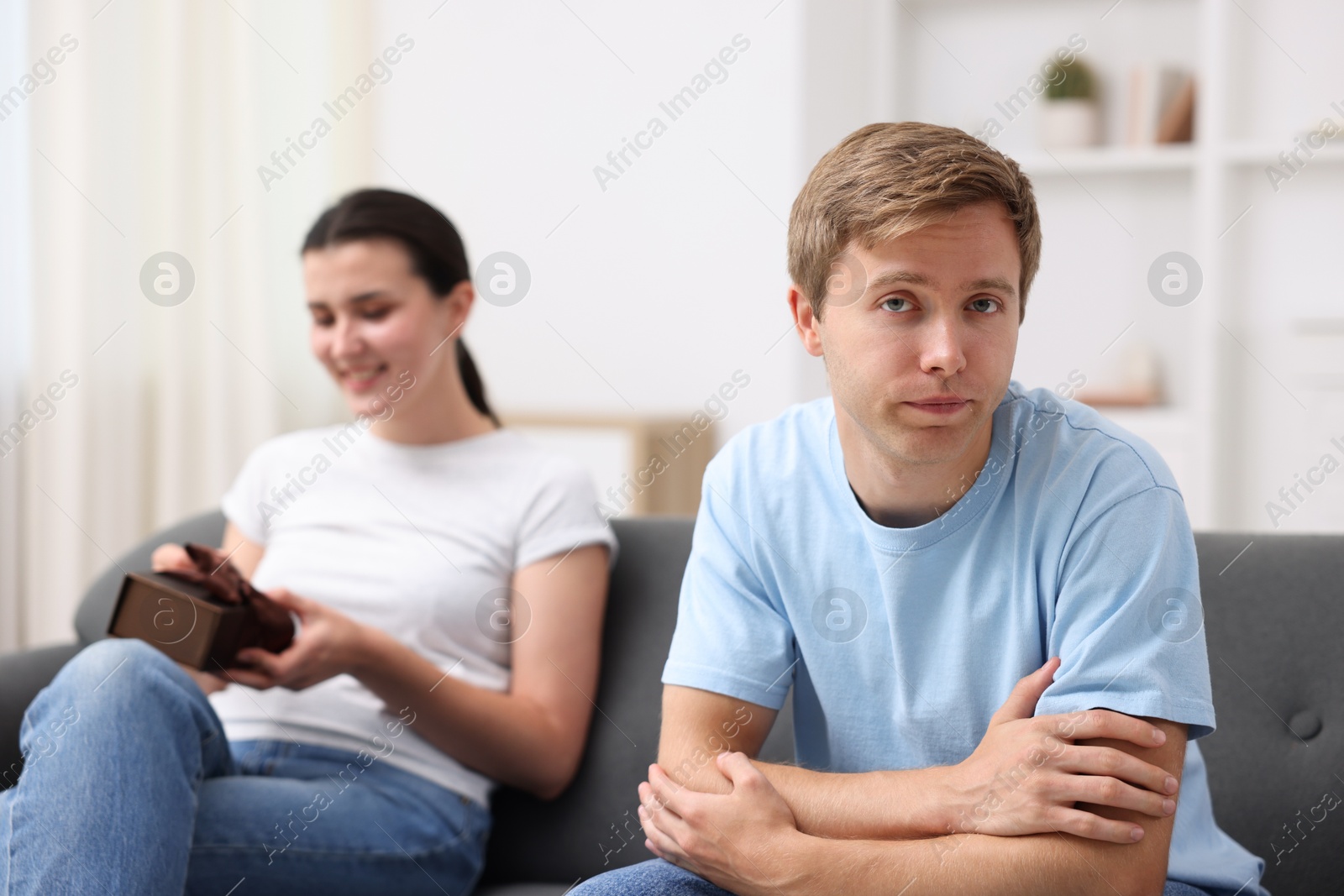 Photo of Man feeling jealous of woman receiving gift at home, selective focus