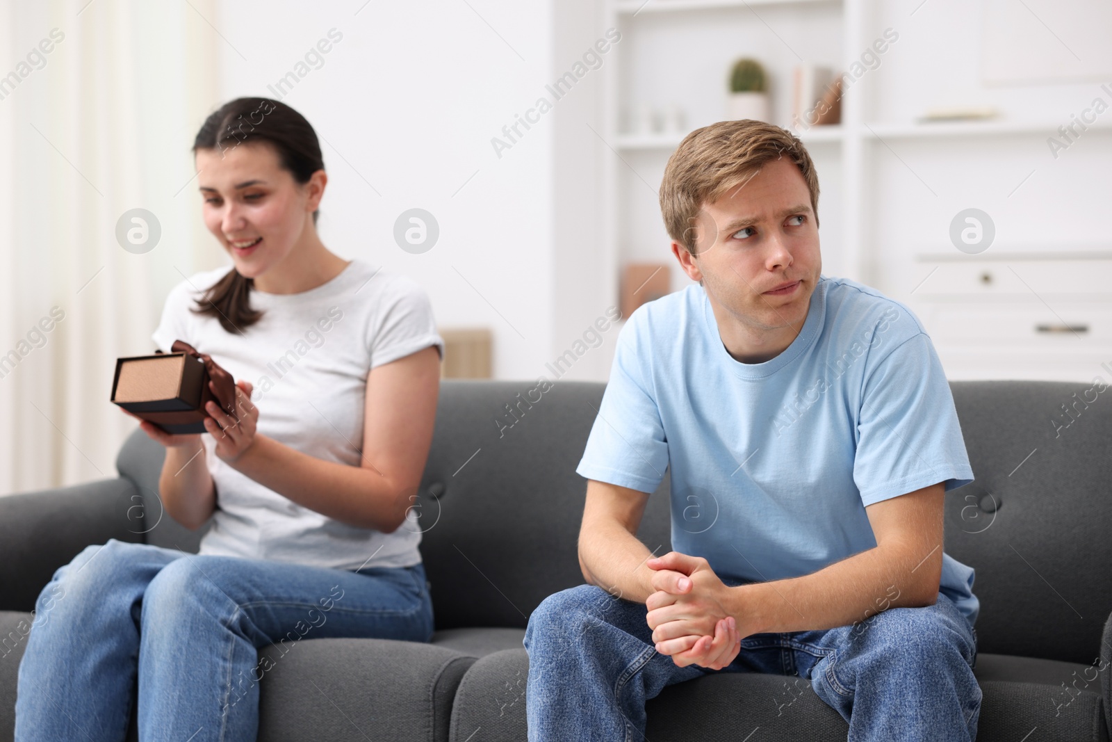 Photo of Man feeling jealous of woman receiving gift at home, selective focus