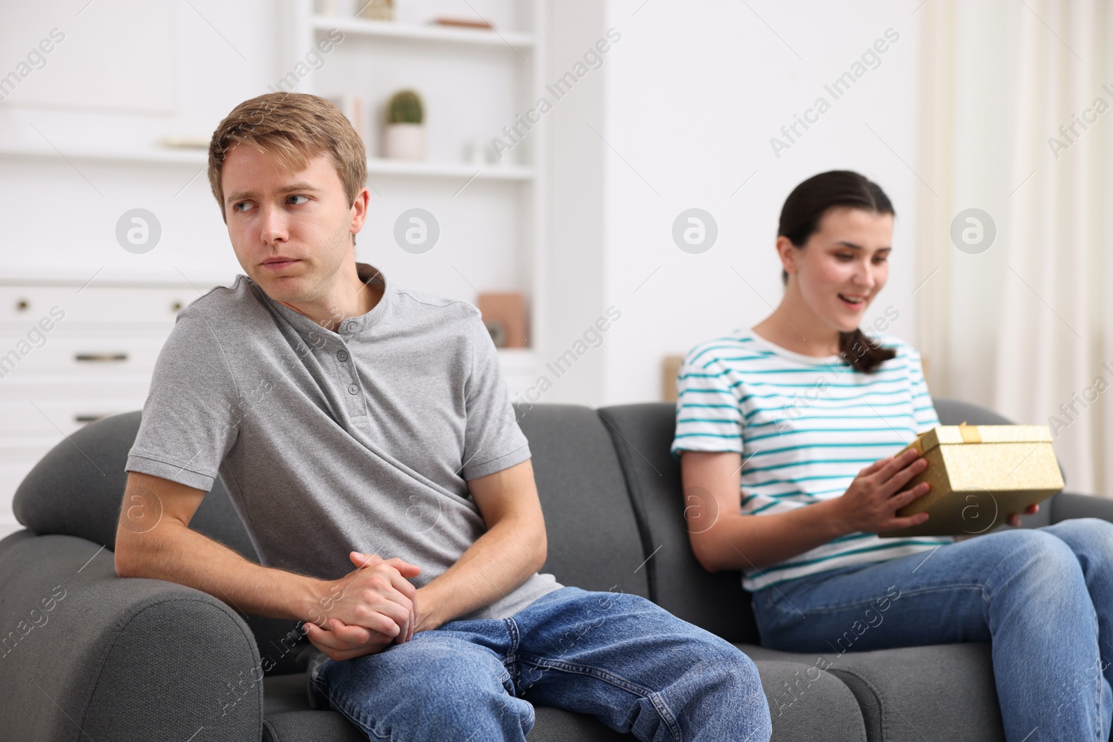 Photo of Man feeling jealous of woman receiving gift at home, selective focus
