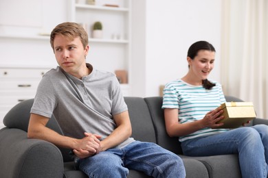 Photo of Man feeling jealous of woman receiving gift at home, selective focus