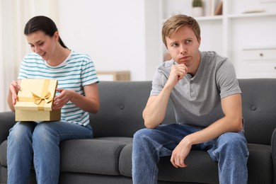 Photo of Man feeling jealous of woman receiving gift at home, selective focus