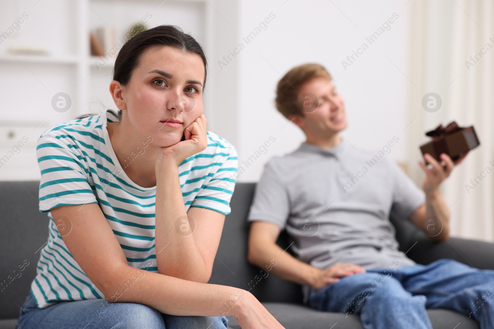 Woman feeling jealous of man receiving gift at home, selective focus Photo of Woman feeling jealous of man receiving gift at home, selective focus