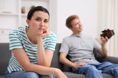 Photo of Woman feeling jealous of man receiving gift at home, selective focus