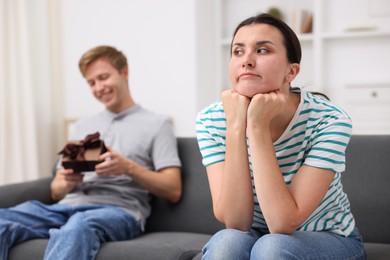 Photo of Woman feeling jealous of man receiving gift at home, selective focus