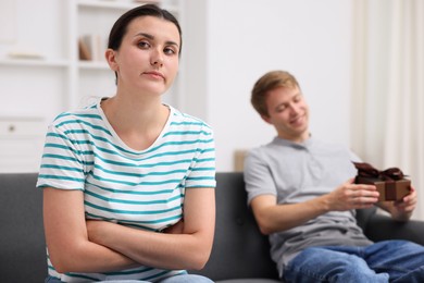 Photo of Woman feeling jealous of man receiving gift at home, selective focus