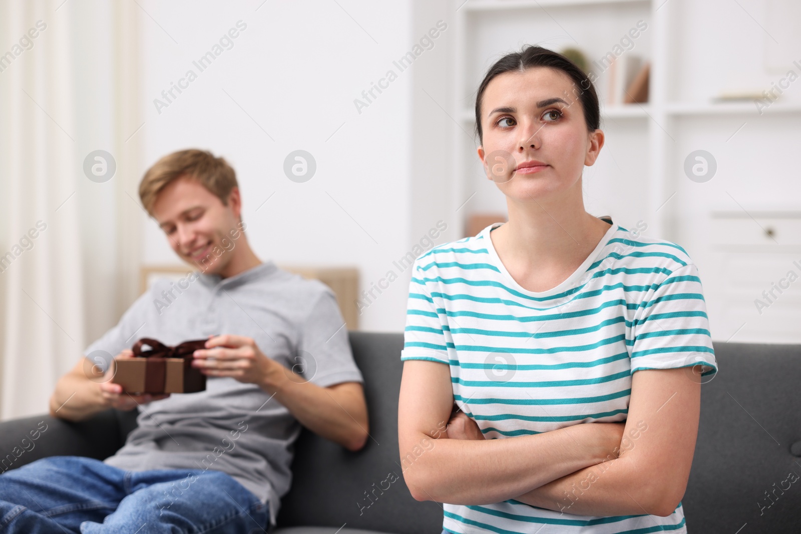 Woman feeling jealous of man receiving gift at home, selective focus Photo of Woman feeling jealous of man receiving gift at home, selective focus