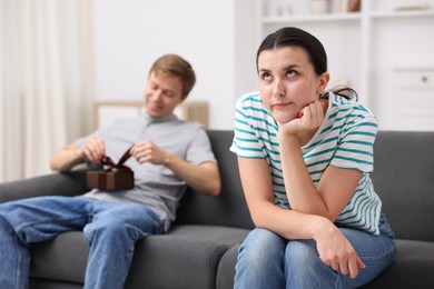 Photo of Woman feeling jealous of man receiving gift at home, selective focus