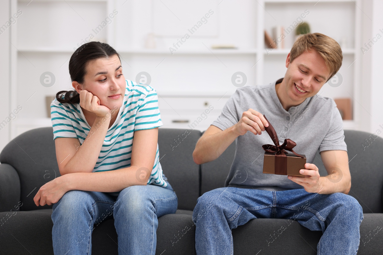 Woman feeling jealous of man receiving gift at home Photo of Woman feeling jealous of man receiving gift at home