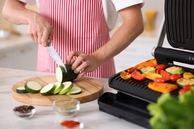Photo of Man cutting zucchini while cooking vegetables on electric grill in kitchen, closeup