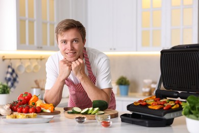 Photo of Man cooking vegetables on electric grill in kitchen