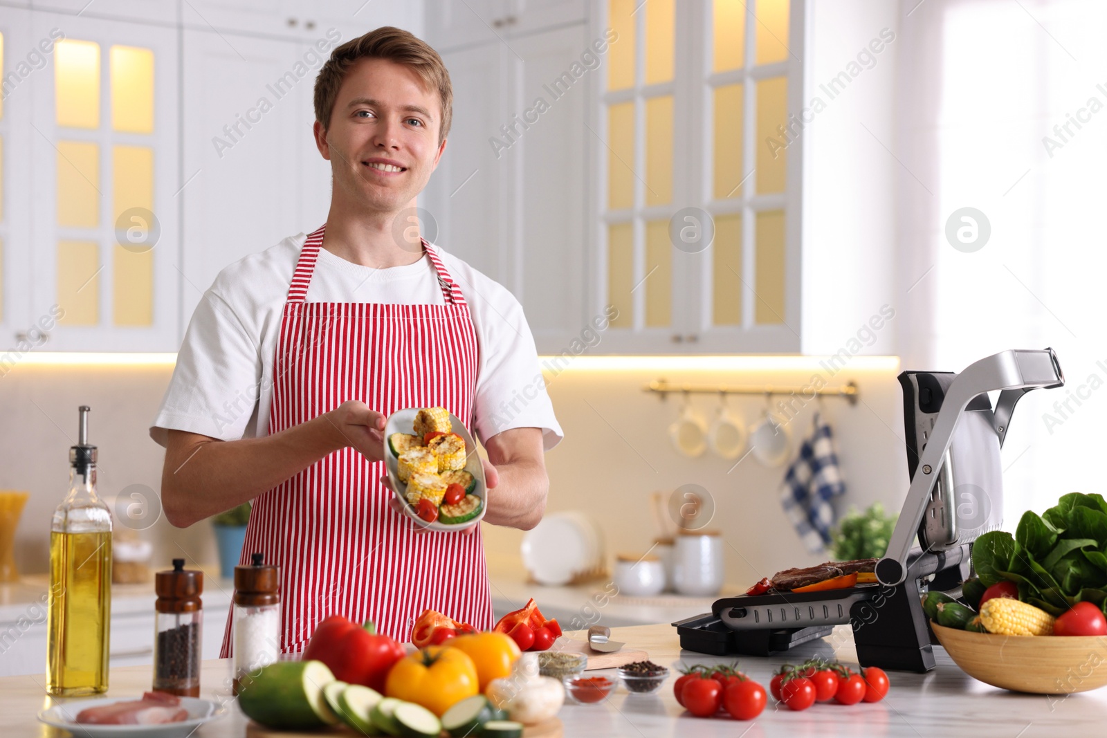 Photo of Man cooking vegetables on electric grill in kitchen