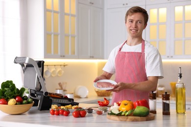 Photo of Man cooking meat and vegetables on electric grill in kitchen