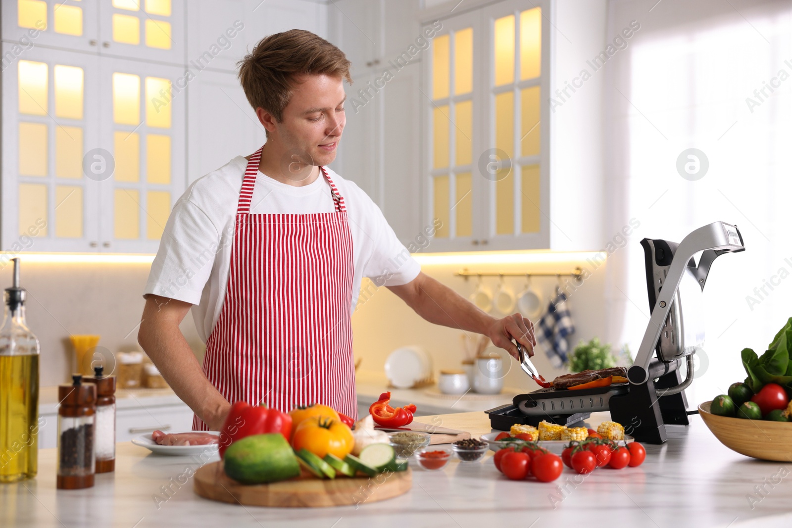 Photo of Man cooking meat and vegetables on electric grill in kitchen