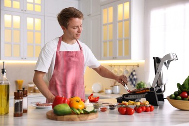 Photo of Man cooking meat and vegetables on electric grill in kitchen