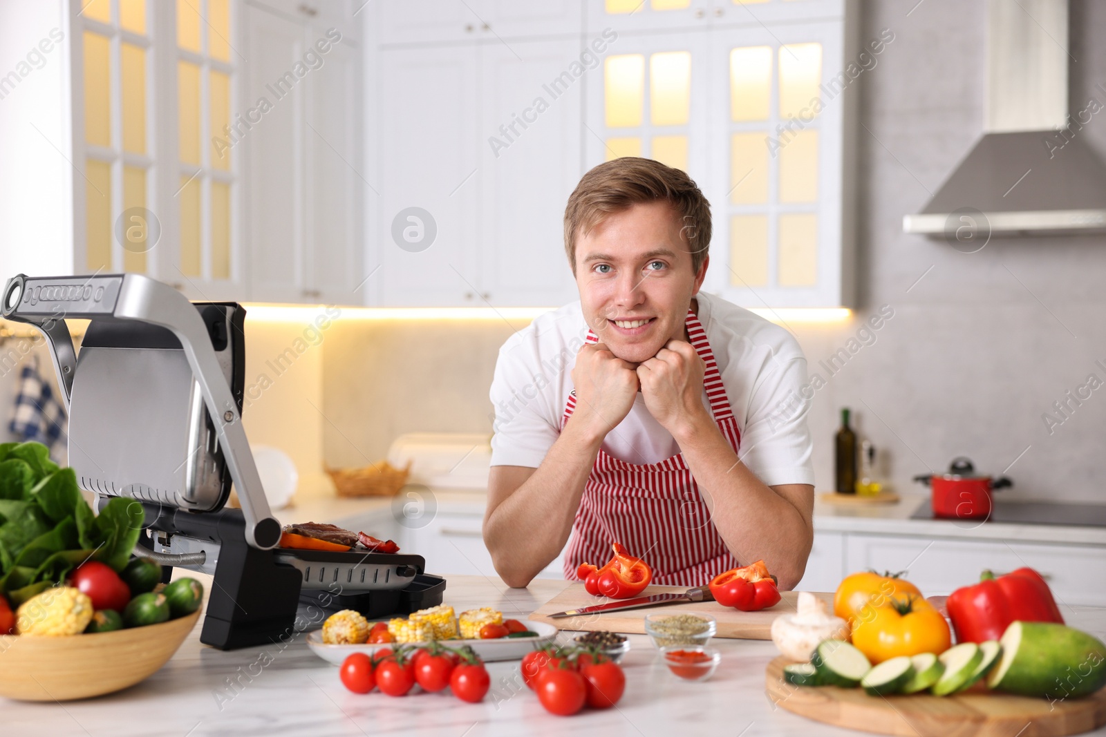 Photo of Man cooking meat and vegetables on electric grill in kitchen