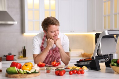 Photo of Man cooking meat and vegetables on electric grill in kitchen