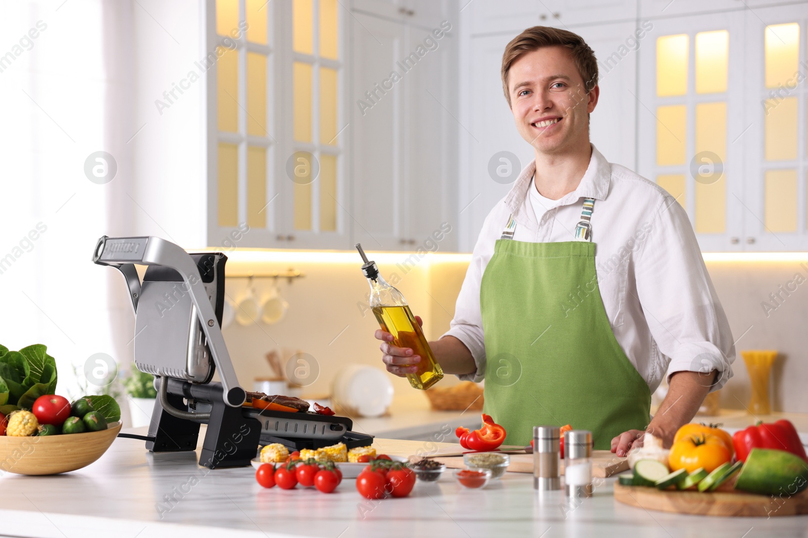 Photo of Man pouring oil onto vegetables cooking on electric grill in kitchen
