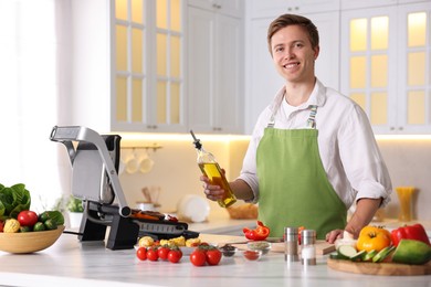 Photo of Man pouring oil onto vegetables cooking on electric grill in kitchen