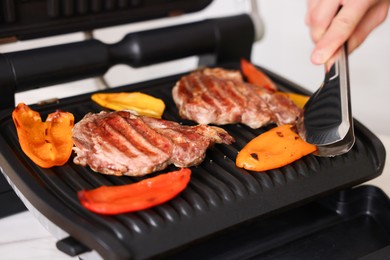 Photo of Man cooking meat and vegetables on electric grill in kitchen, closeup