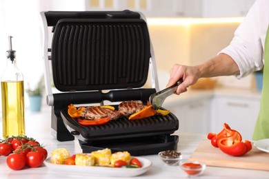 Photo of Man cooking meat and vegetables on electric grill in kitchen, closeup