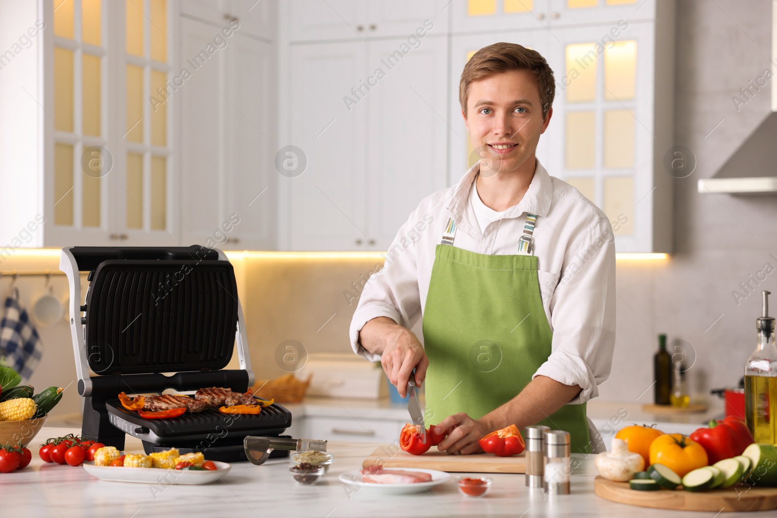 Photo of Man cutting pepper while cooking vegetables on electric grill in kitchen