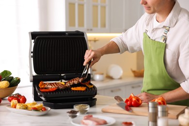 Photo of Man cooking meat and vegetables on electric grill in kitchen, closeup