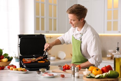 Photo of Man cooking meat and vegetables on electric grill in kitchen