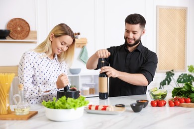 Photo of Smiling man opening bottle of wine while cooking with his wife at table in kitchen