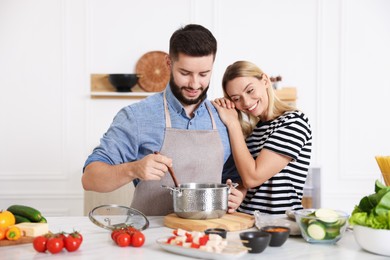 Photo of Happy couple cooking together at table in kitchen