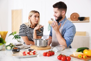 Photo of Happy couple talking while cooking together at table in kitchen