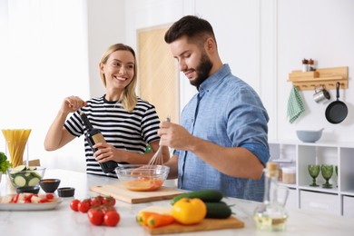 Photo of Smiling woman opening bottle of wine while cooking with her husband at table in kitchen