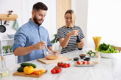 Photo of Smiling woman opening bottle of wine while cooking with her husband at table in kitchen