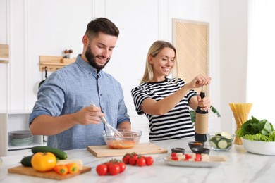 Photo of Smiling woman opening bottle of wine while cooking with her husband at table in kitchen