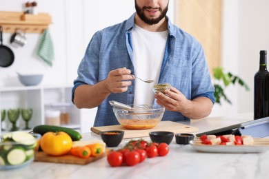 Photo of Cooking process. Smiling man seasoning dish at table in kitchen, closeup