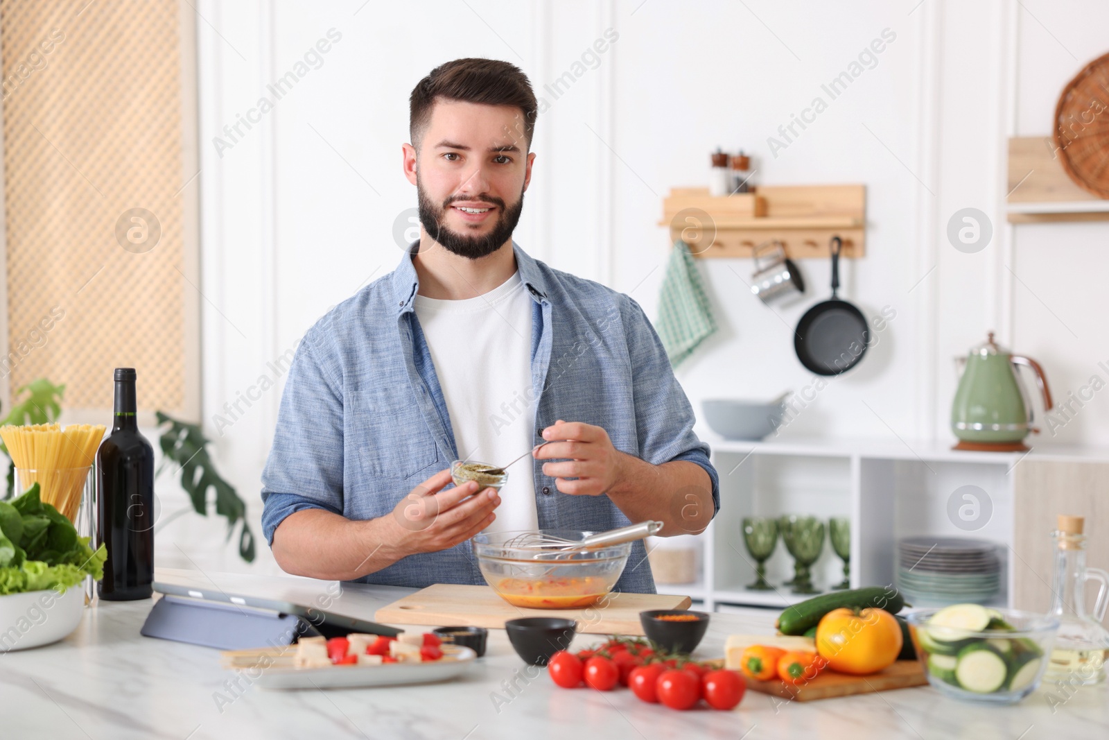 Photo of Cooking process. Smiling man seasoning dish at table in kitchen