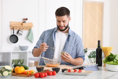 Photo of Cooking process. Young man seasoning dish at table in kitchen