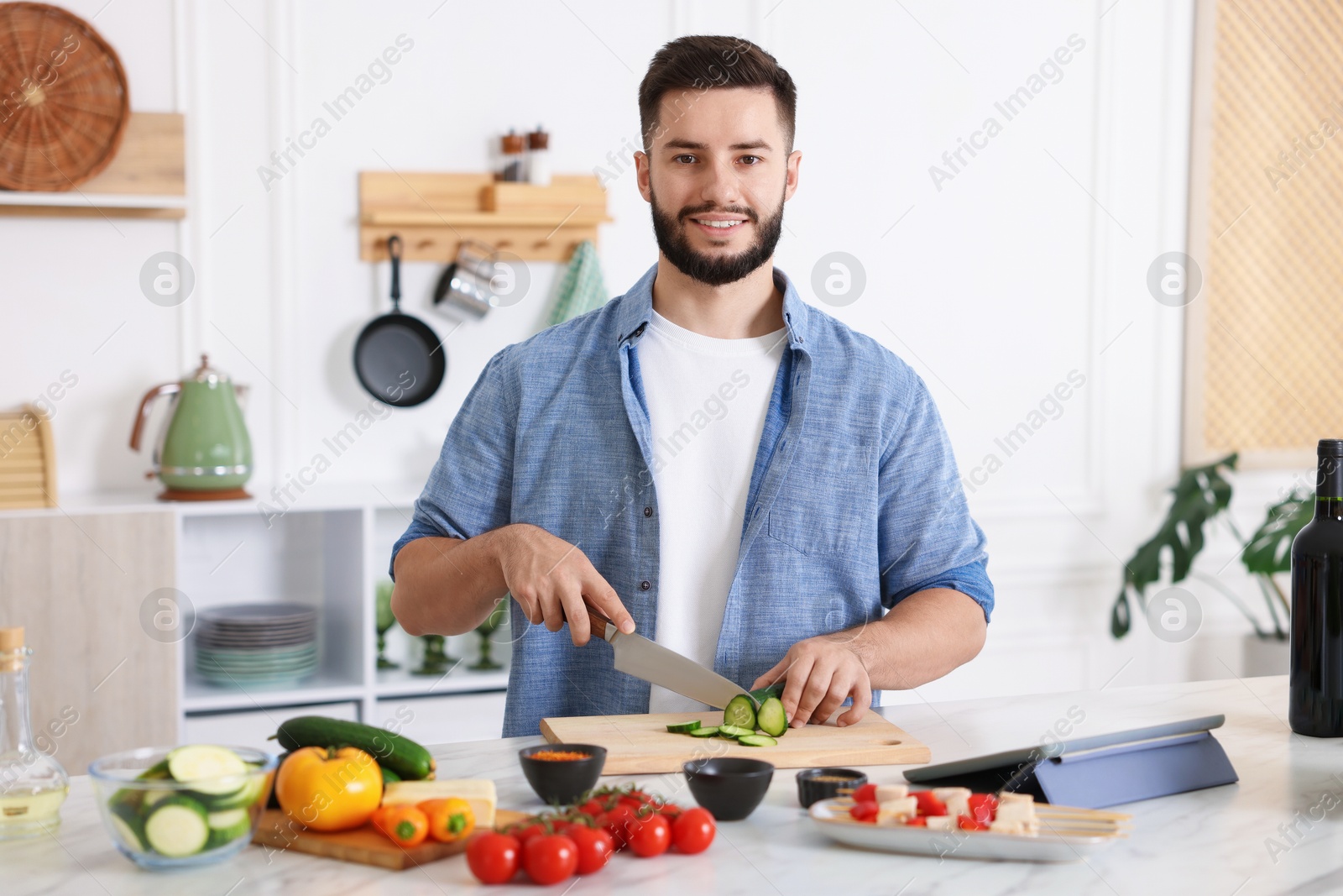 Photo of Cooking process. Smiling man cutting cucumber at table in kitchen