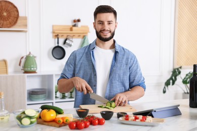 Photo of Cooking process. Smiling man cutting cucumber at table in kitchen