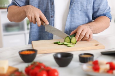 Photo of Cooking process. Man cutting cucumber at table indoors, closeup