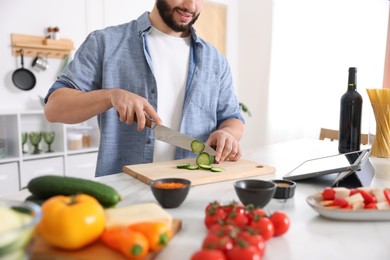 Photo of Cooking process. Smiling man cutting cucumber at table in kitchen, closeup